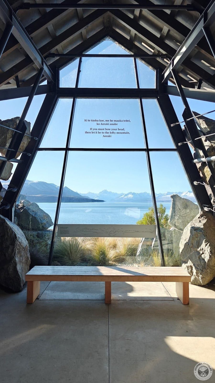 bench in front of a huge glass window with a view of the lake and mountain