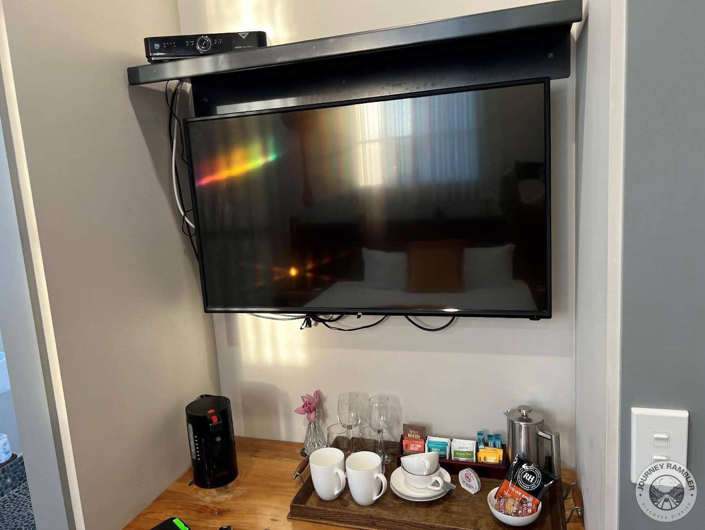 coffee machine, a kettle, some tea and coffee sachets, cups, mugs, glasses and cookies had all been arranged on a shelf under the TV