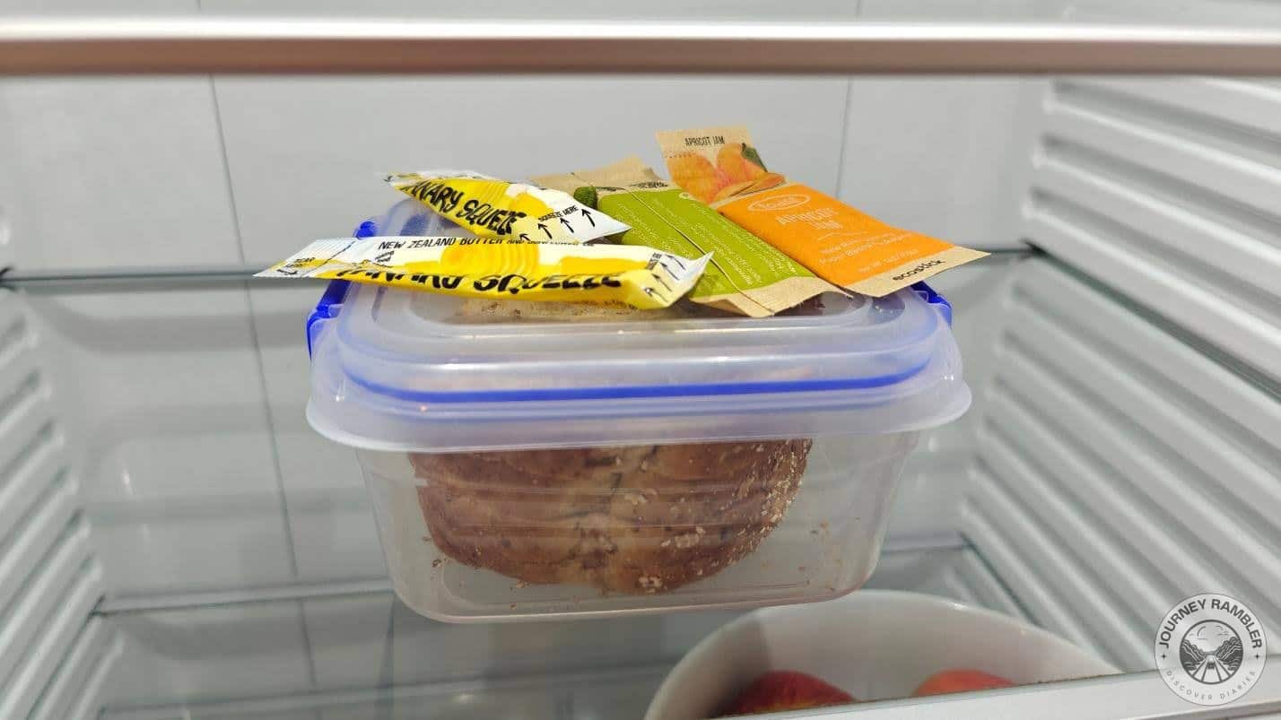 some jam sachets and a plastic box with some multigrain bread