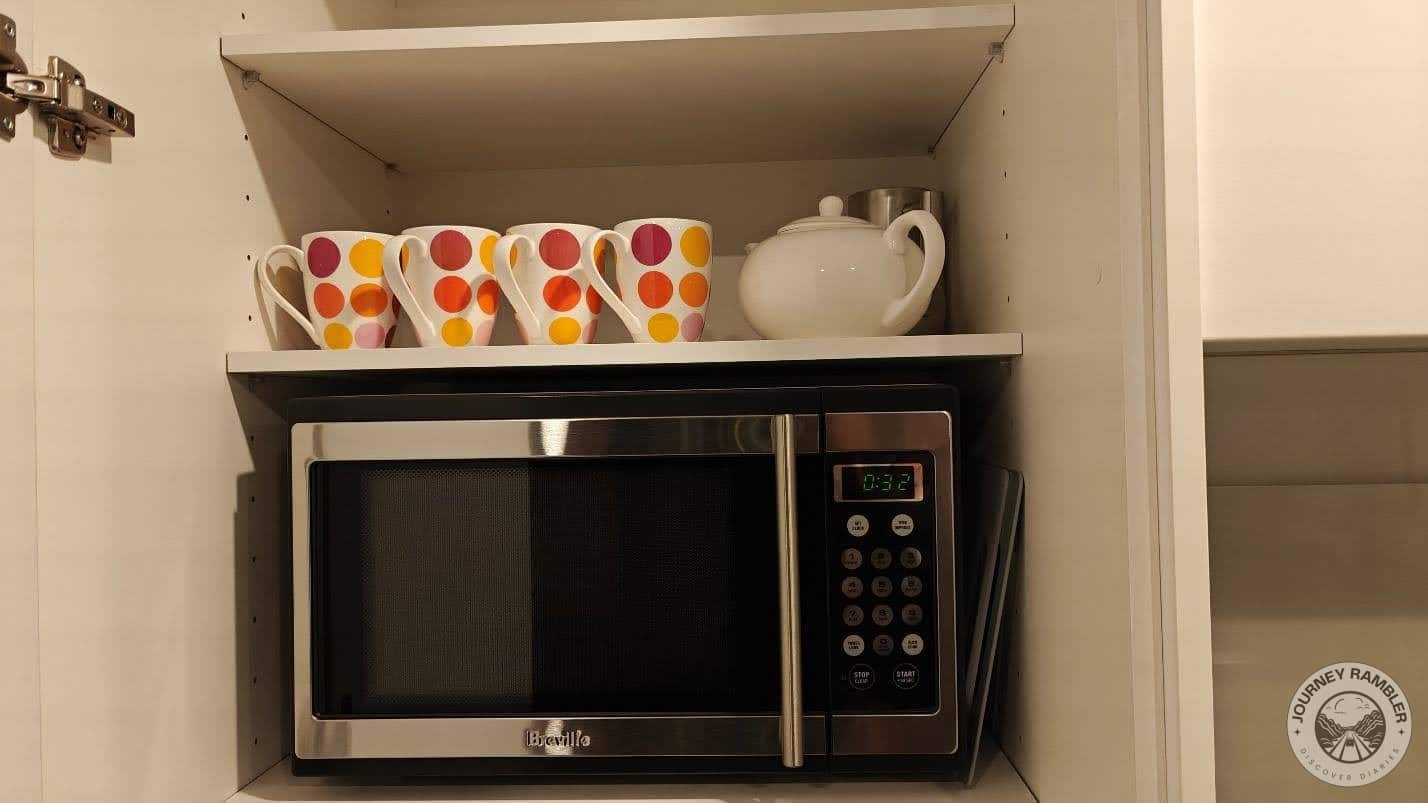 teapot and four colorful mugs had been placed on a shelf above the microwave