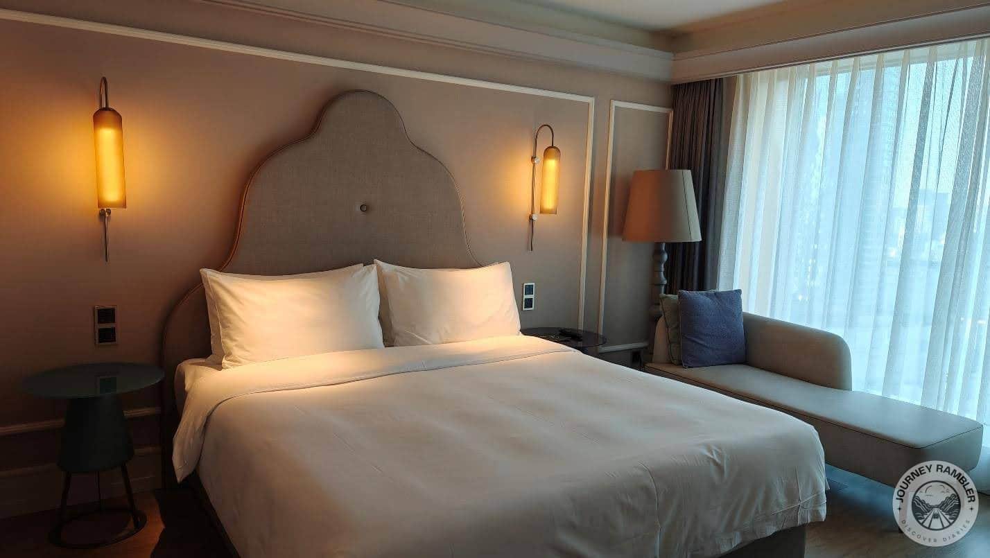 comfortable double bed with four pillows and a long couch next to the window