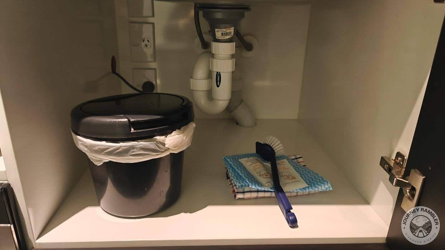 cupboard below the washbasin held cleaning supplies and a wastepaper basket