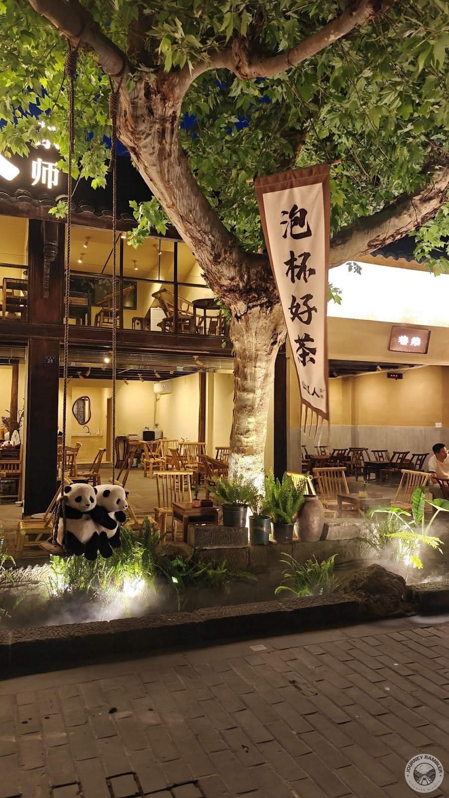 pair of pandas on a swing right outside a restaurant