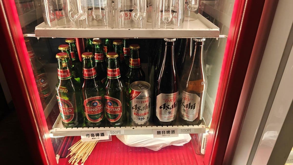 Beer bottles and cans on a fridge shelf, Tsingtao and Asahi brands.