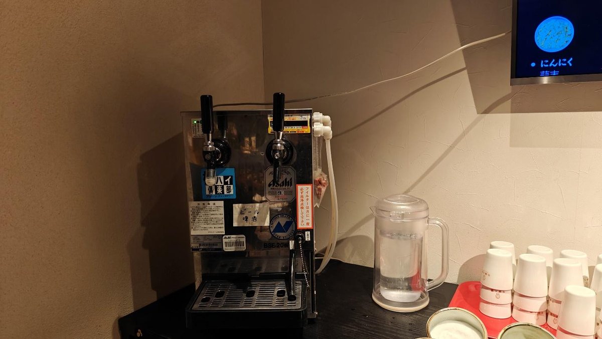 Beer dispenser with taps, water pitcher, and stacked cups on the counter.