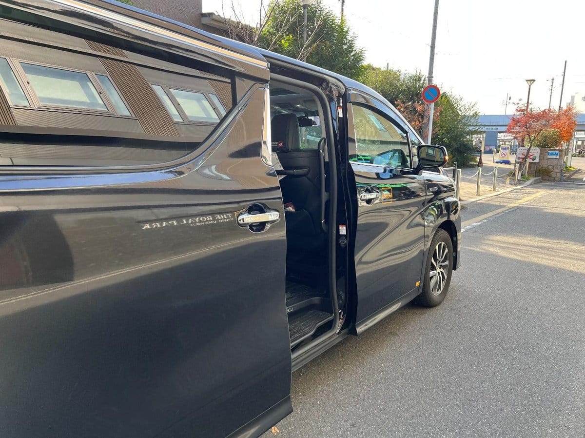 Black van with sliding door open on a sunny street.