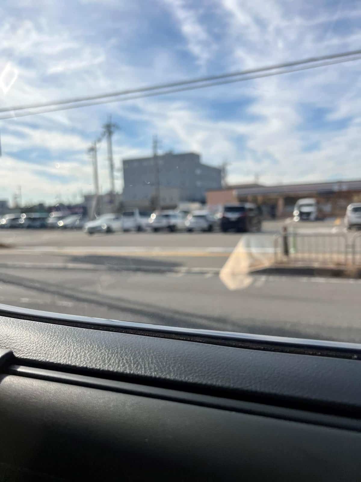 Blurred view of parking lot and building through car window, sunny sky.