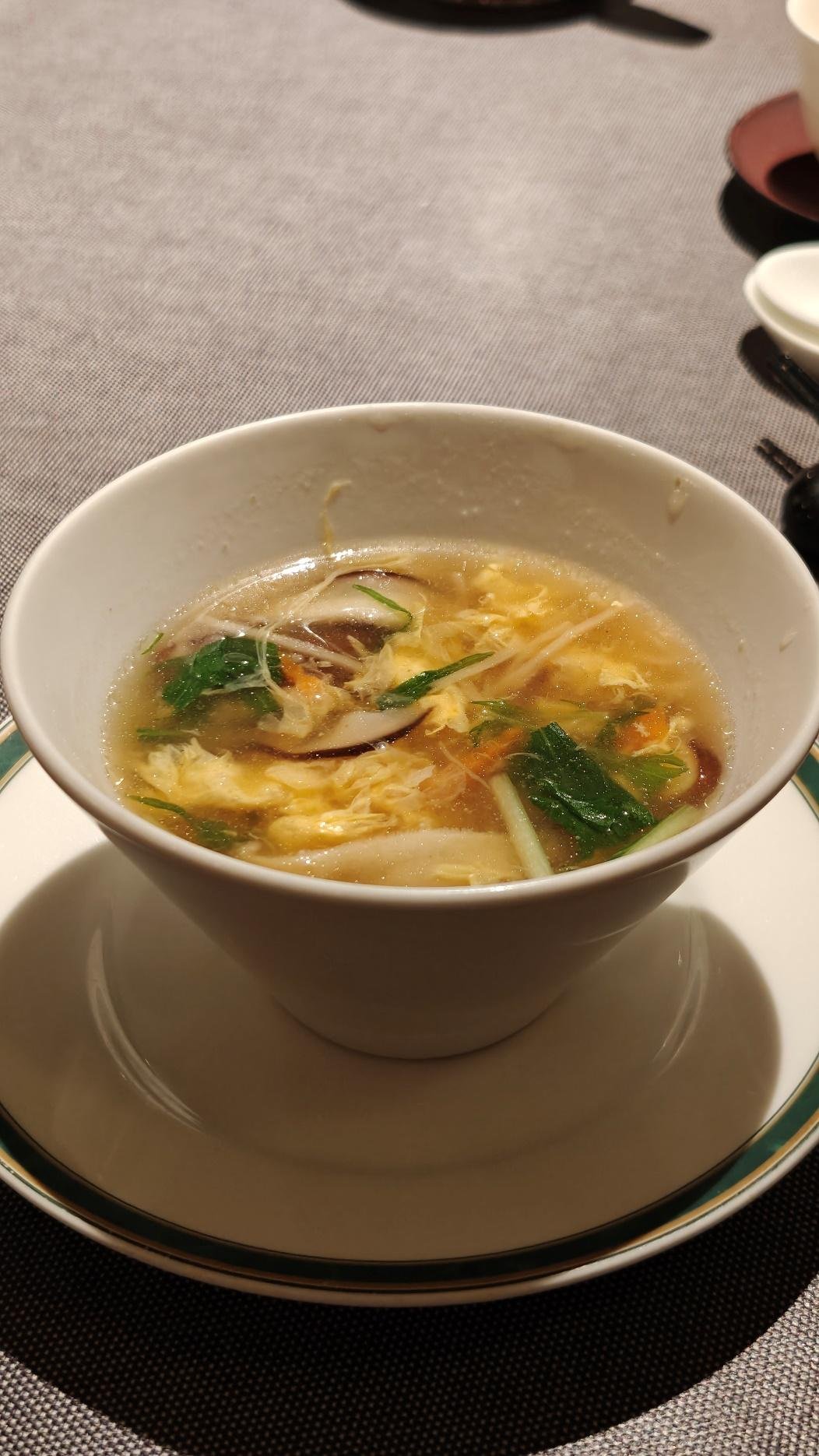 Bowl of hot soup with leafy greens and mushrooms on a table setting.