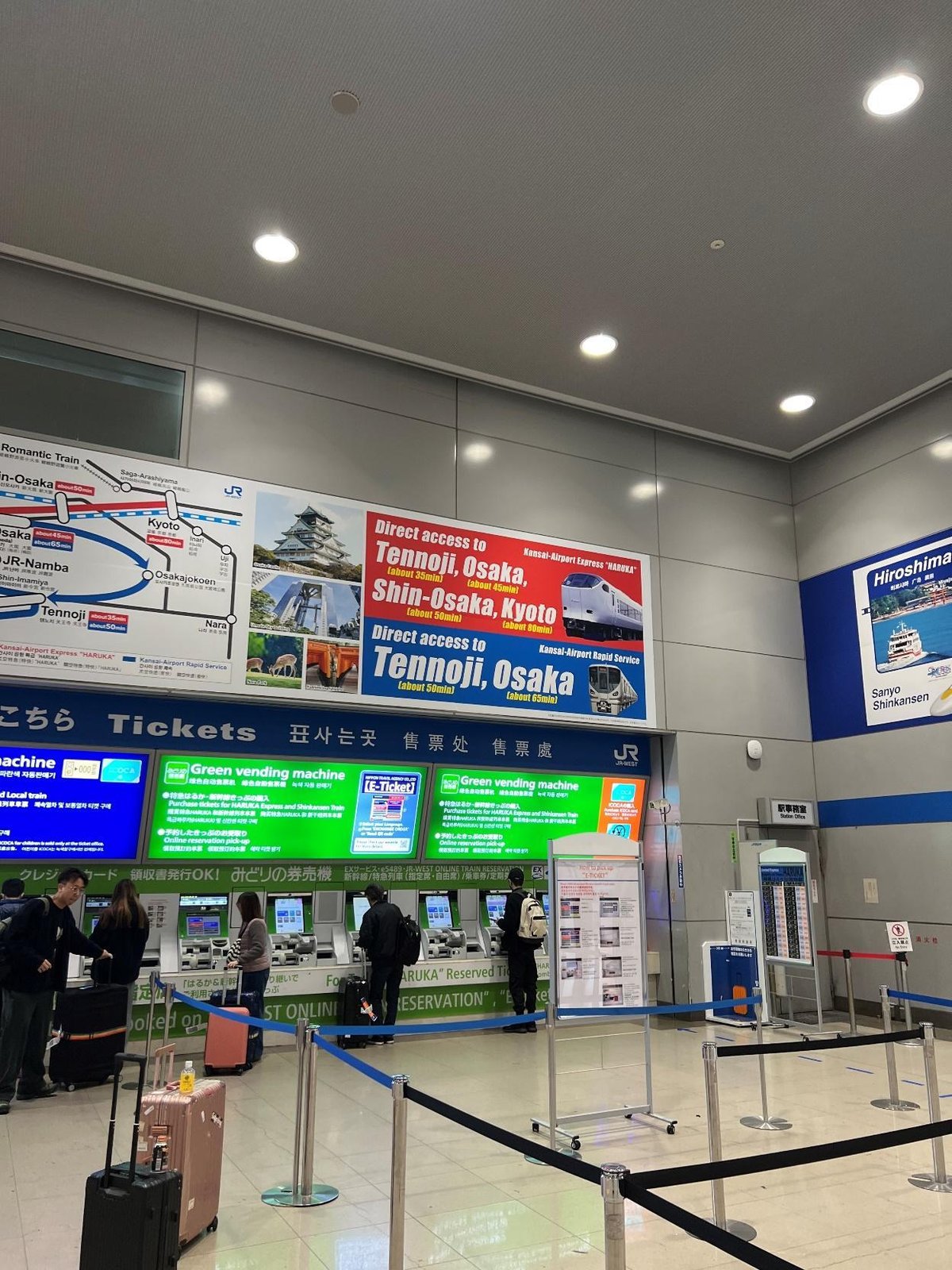 Busy train station ticket area with travelers and bright signage.
