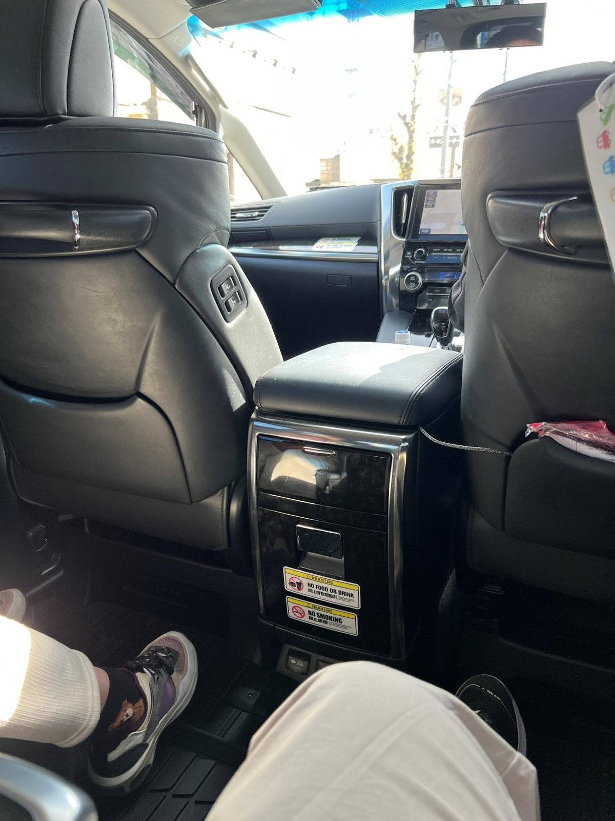 Car interior with leather seats and passenger wearing sneakers.