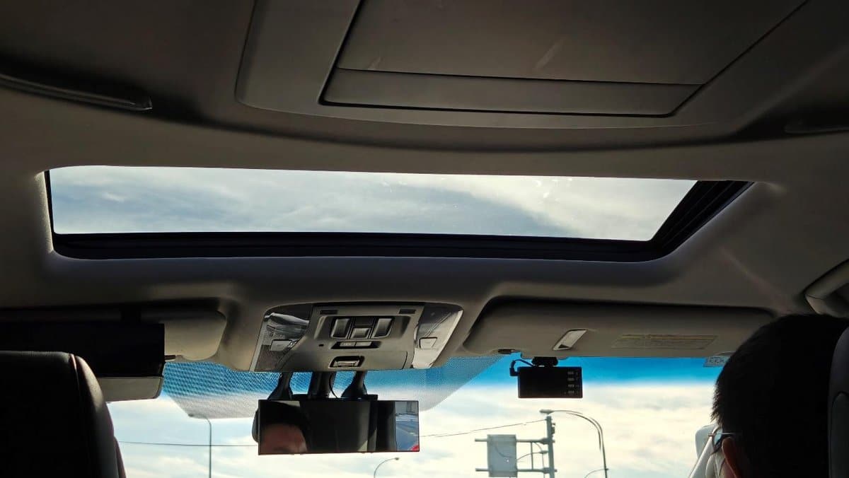 Car sunroof view with blue sky and clouds above.