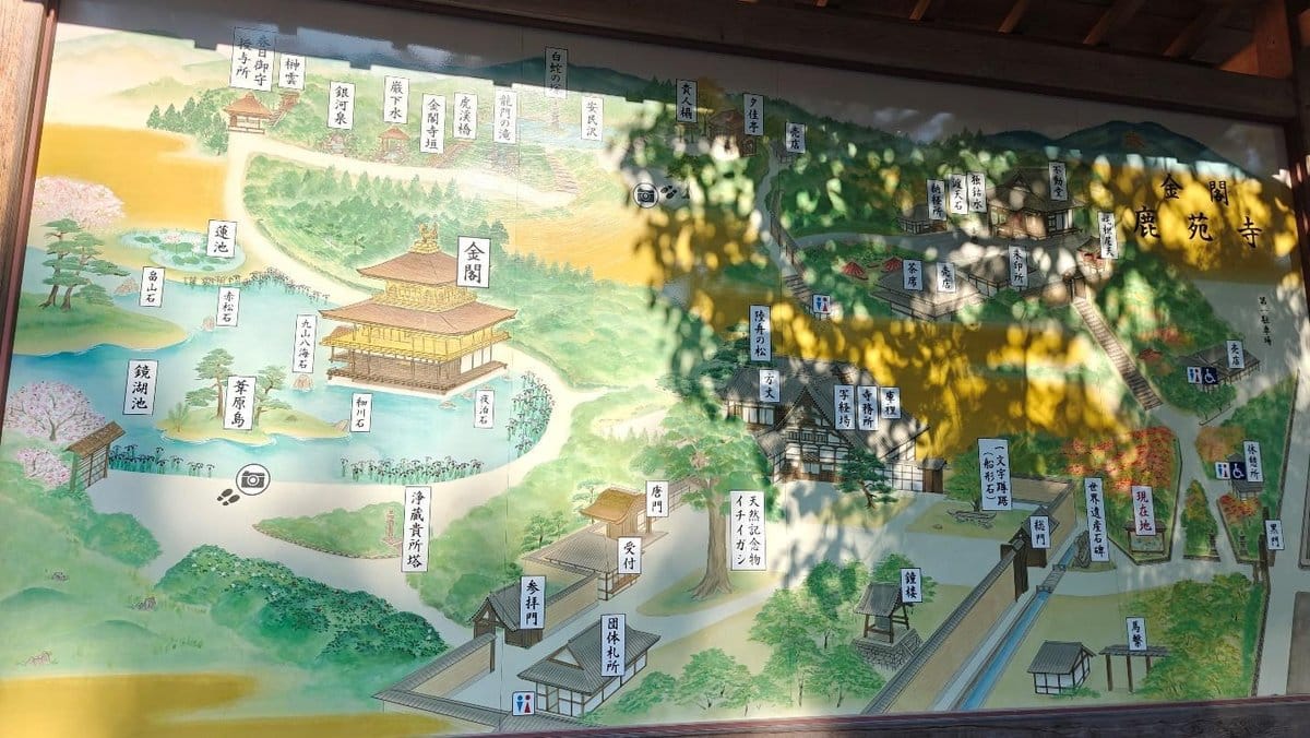 Colorful map of Kinkaku-ji, labeled in Japanese, under dappled sunlight.