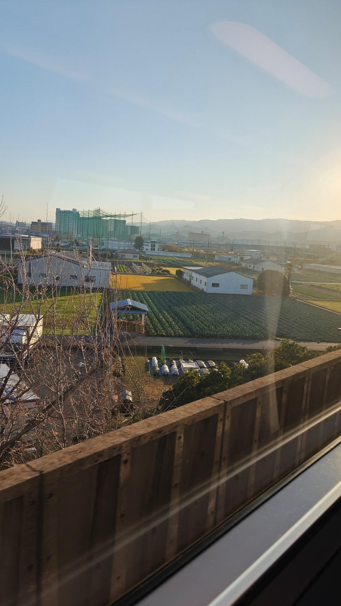 Countryside fields and buildings under a clear blue sky at sunset.