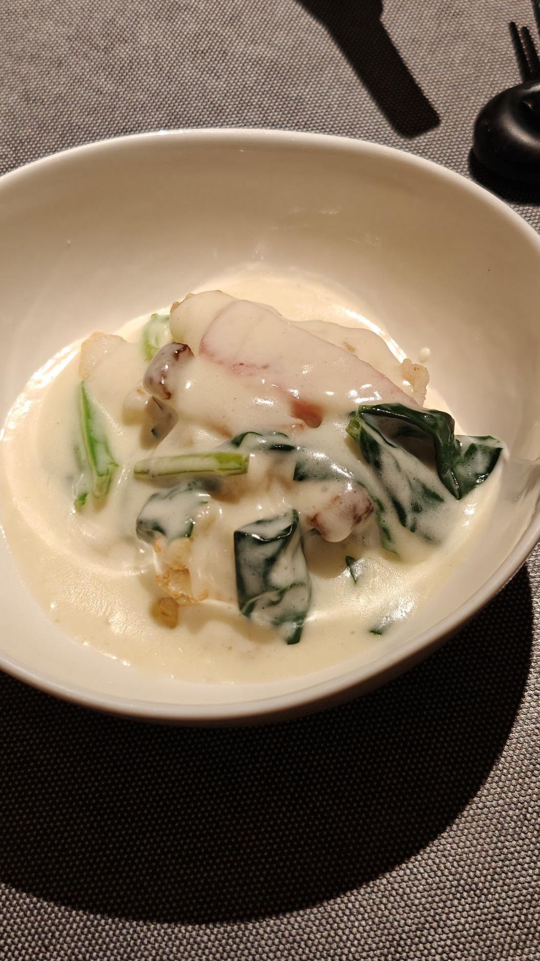 Creamy seafood dish with greens in white bowl on gray tablecloth.