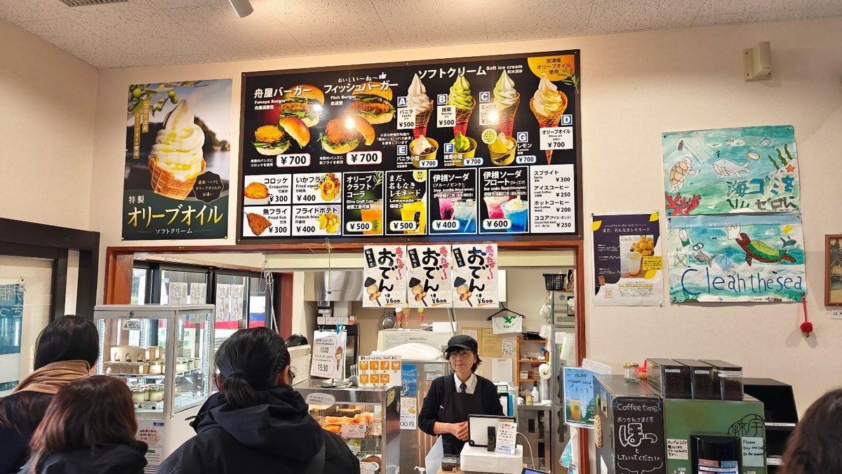 Customers wait at a Japanese cafe counter with menu boards overhead.