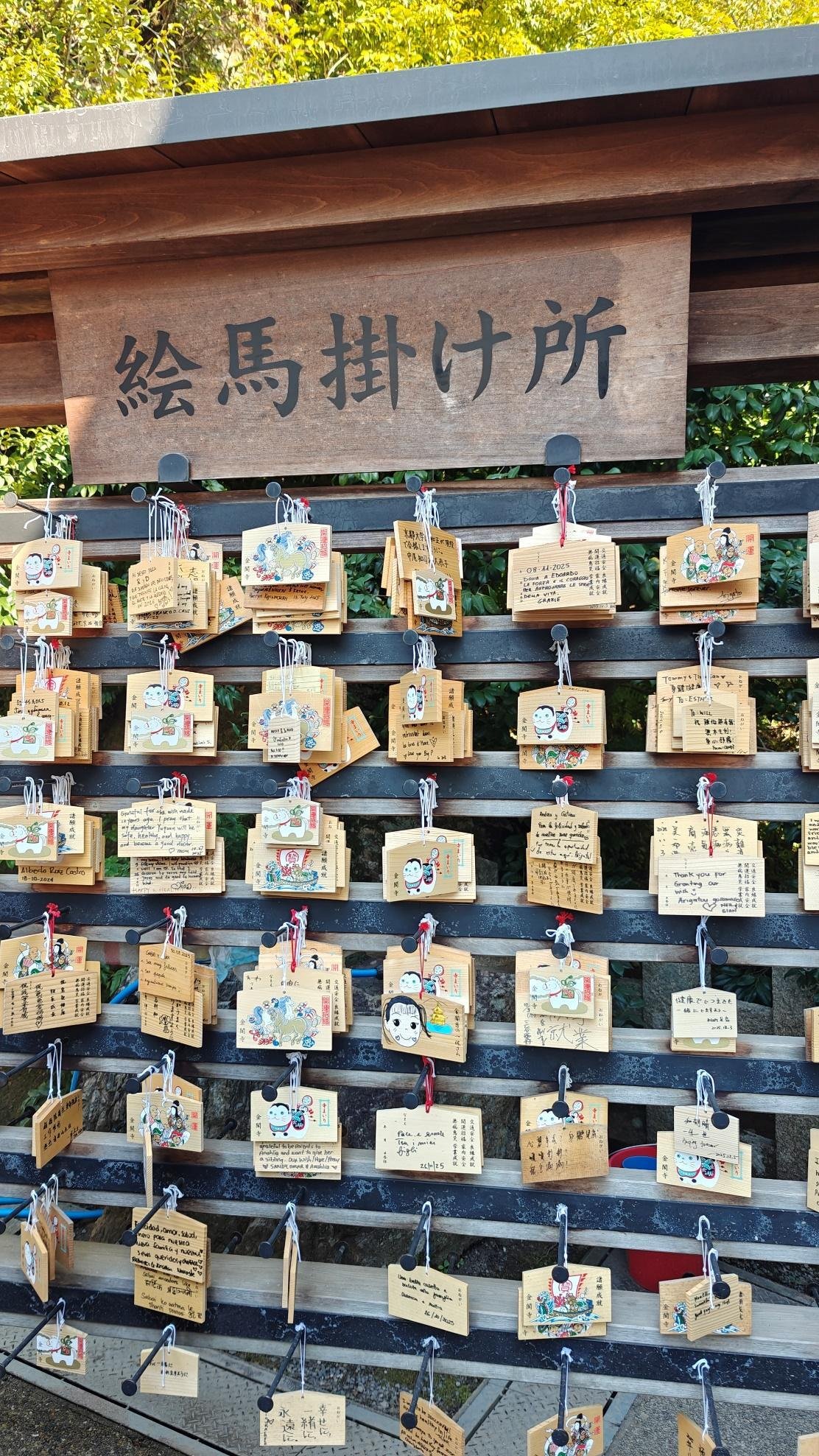Ema plaques hanging on wooden racks in a sunny outdoor shrine setting.