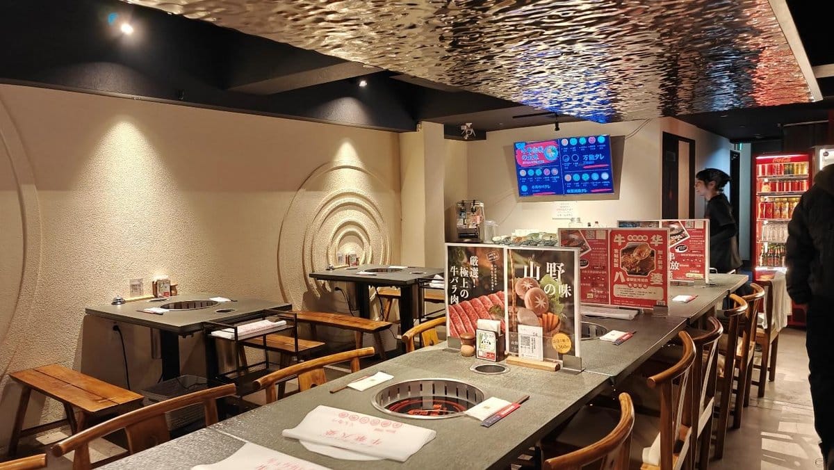 Empty restaurant with wooden chairs, grill tables, and colorful menu signs.