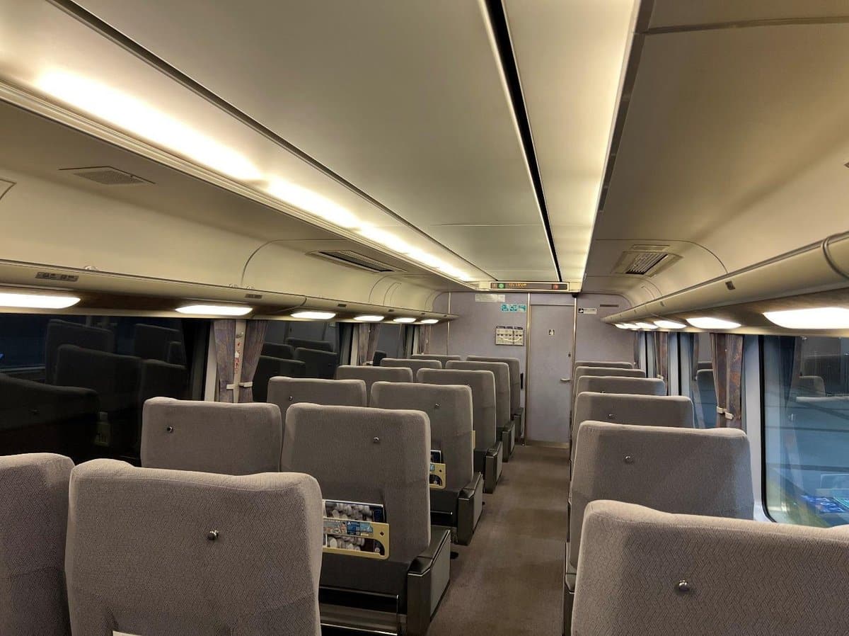 Empty train cabin with gray seats, overhead lighting, and clean aisles.