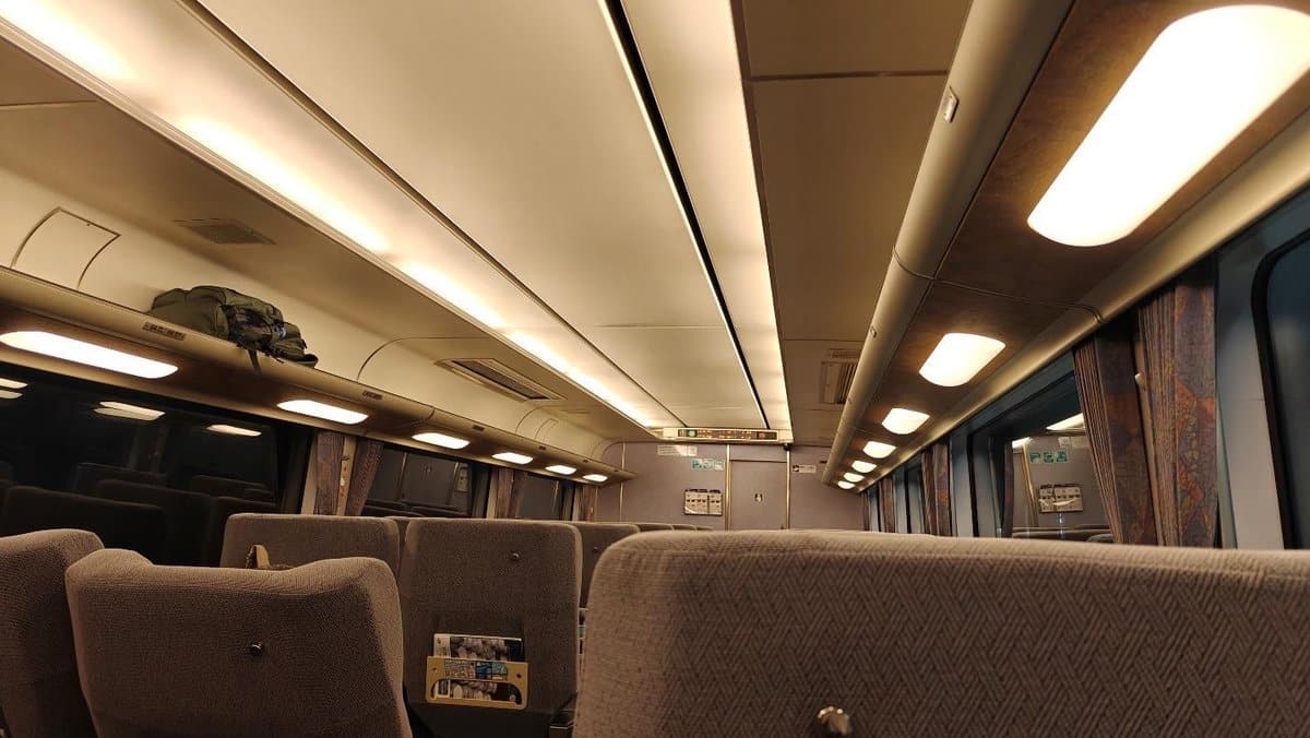 Empty train interior with overhead lights and luggage rack.