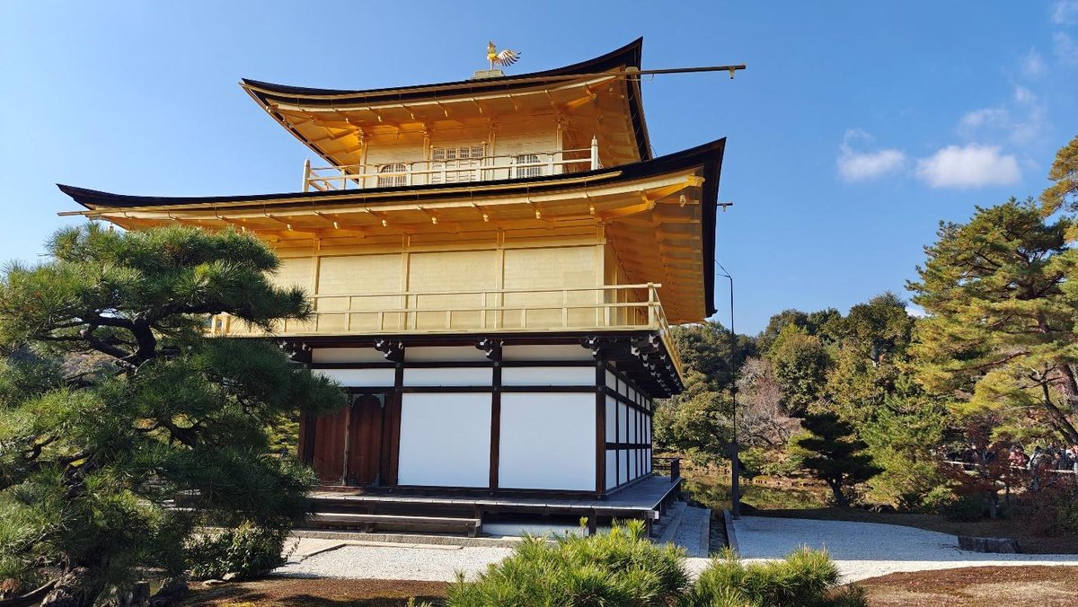 Golden Japanese temple with lush greenery and clear blue sky.