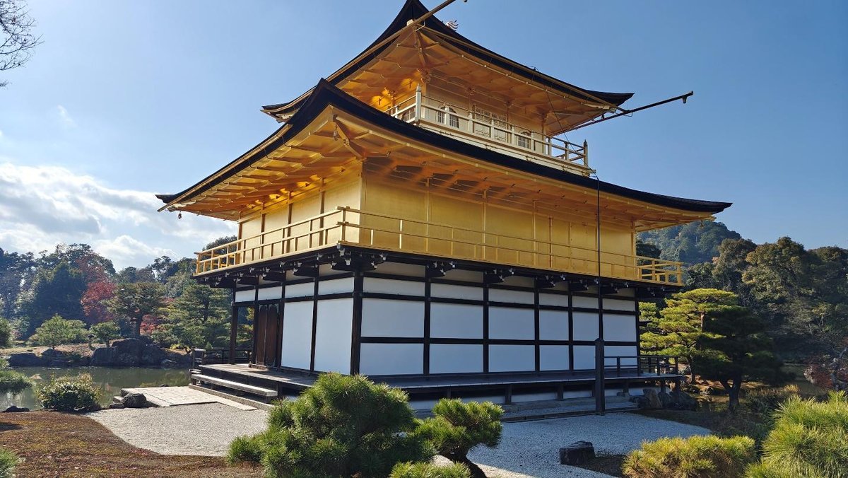Golden pavilion with tiered roof, surrounded by trees and blue sky.