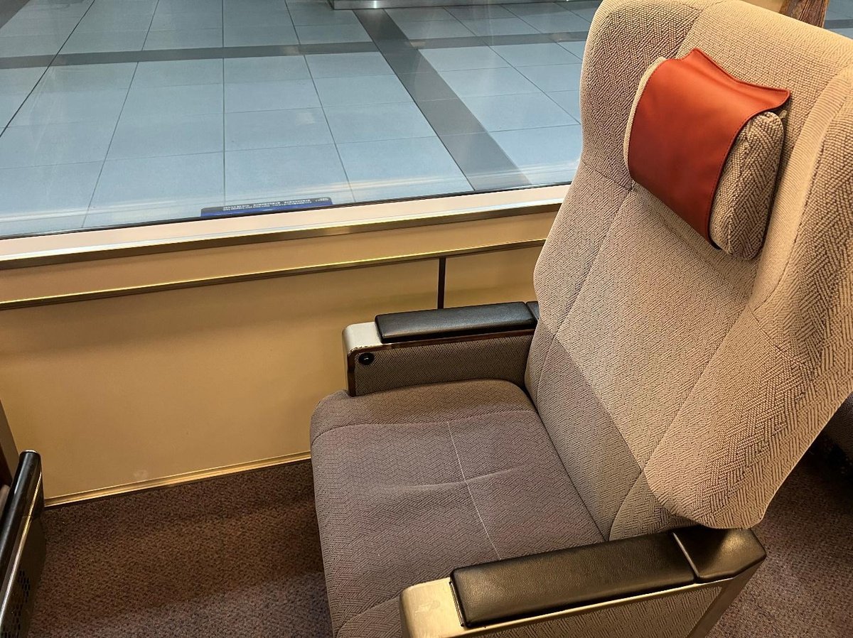 Gray train seat with red headrest, facing a large window.