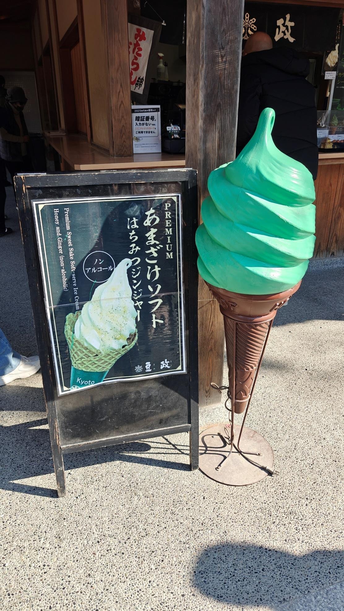 Green ice cream cone sculpture next to a menu sign on a sunny street.