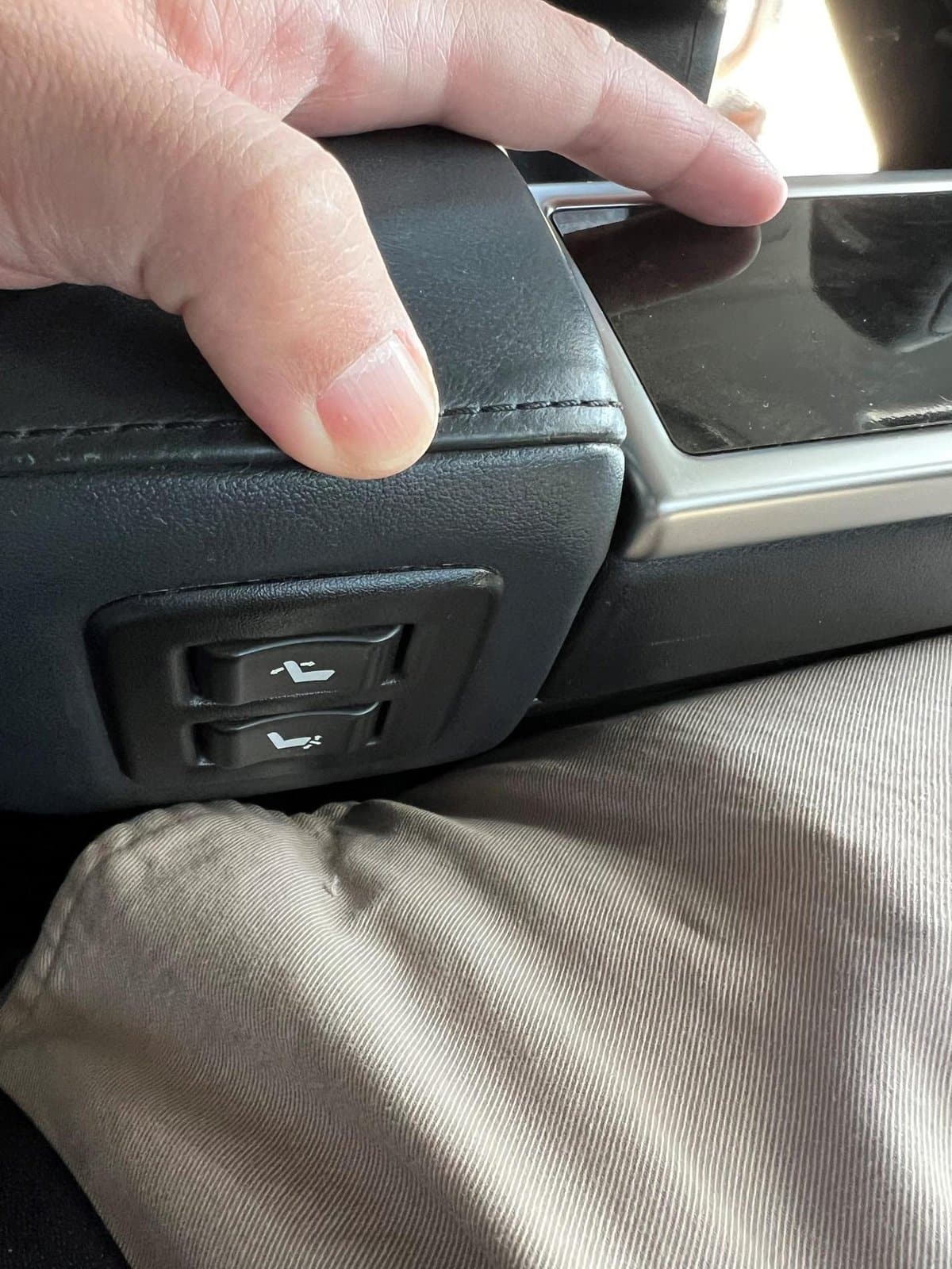 Hand adjusting car seat position using buttons on armrest.