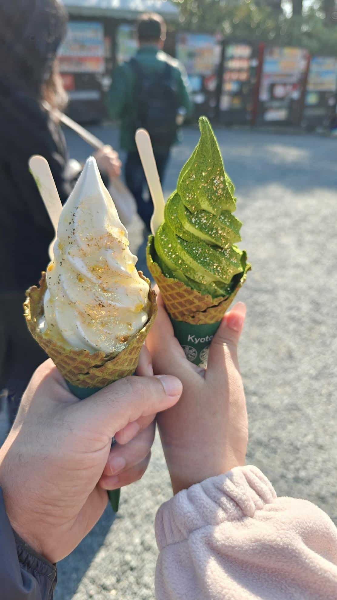 Hands holding matcha and vanilla ice cream cones with gold sprinkles.