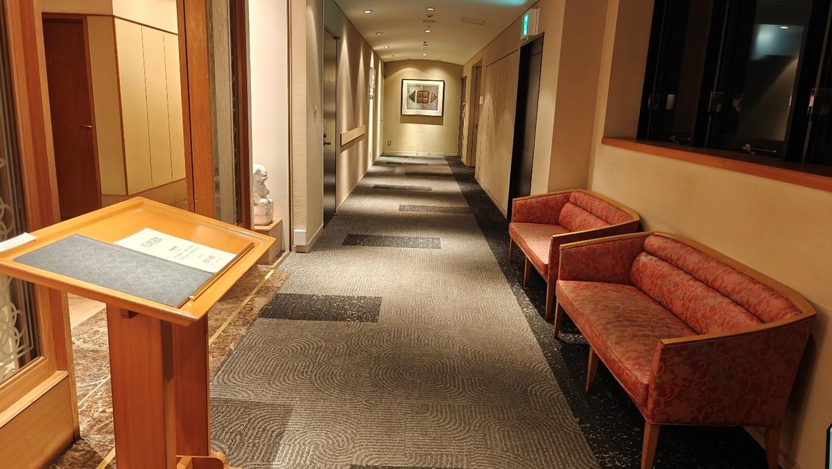 Hotel hallway with patterned carpet, red sofas, and painting on wall.