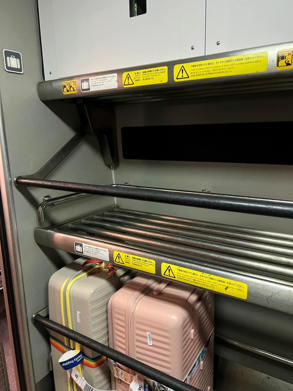 Luggage rack with pastel suitcases secured by a colorful strap.