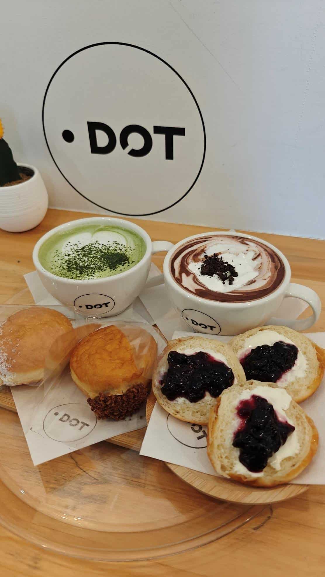 Matcha latte, hot chocolate, buns, and scones on a wooden table.
