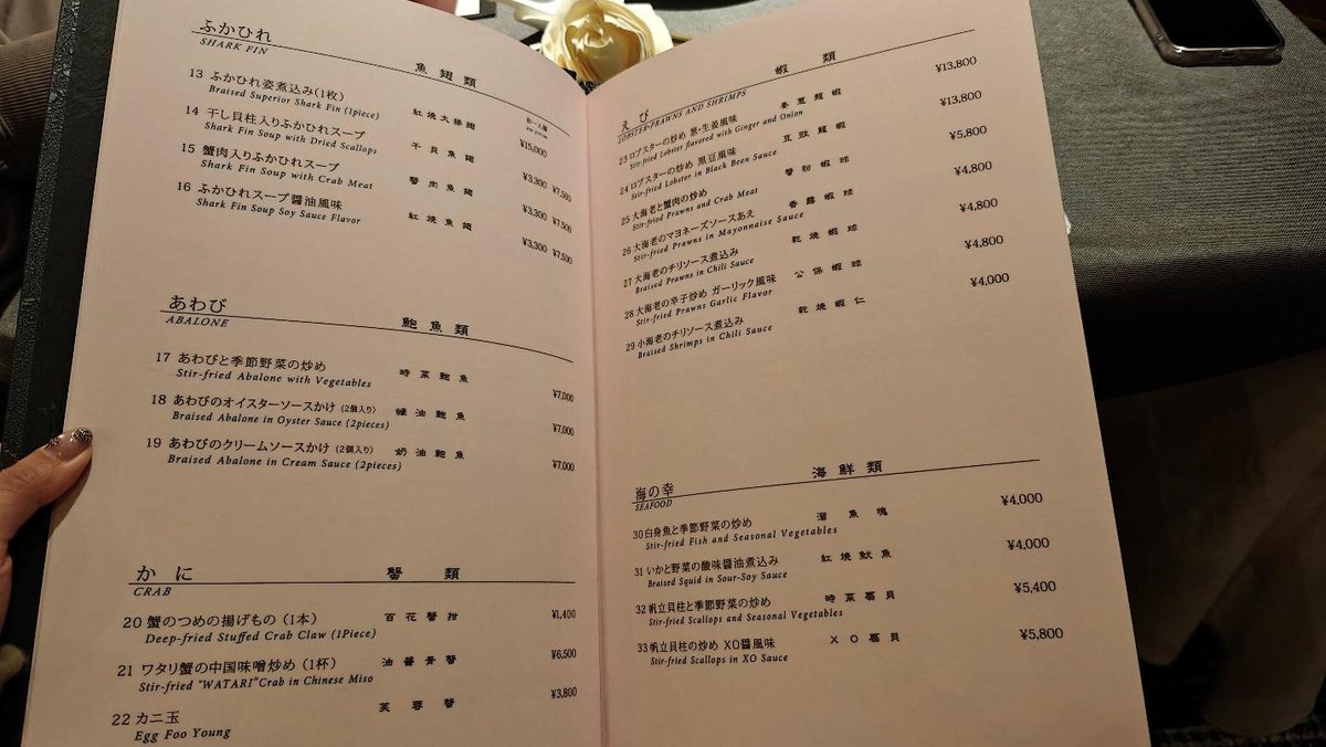 Open menu on a table, listing dishes like shark fin and abalone.