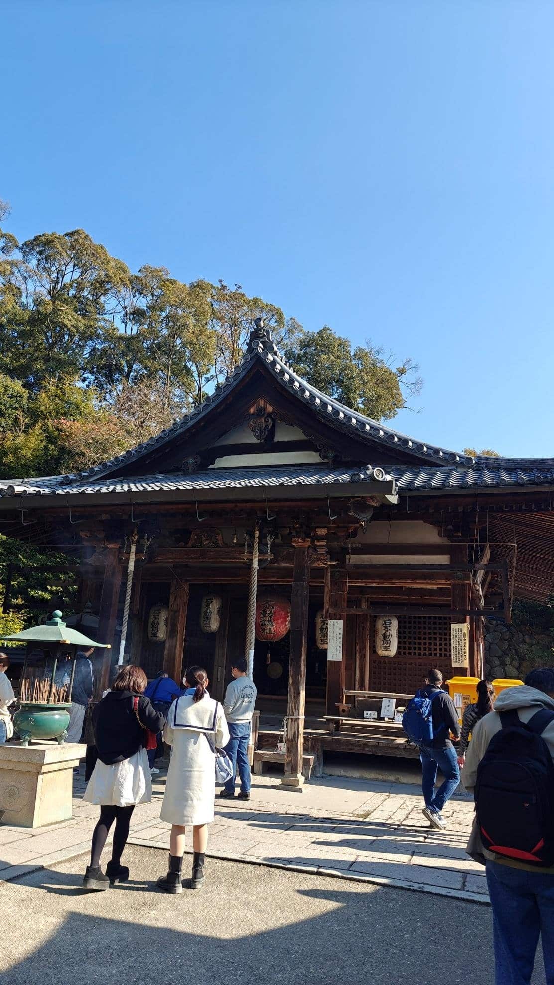 People visit traditional wooden temple under clear blue sky.