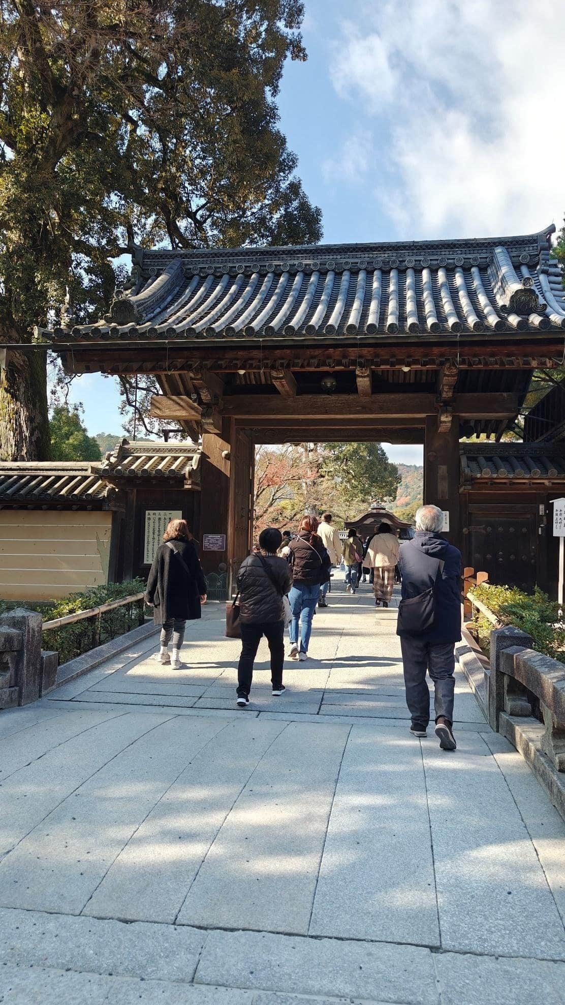 People walking through traditional Japanese wooden gate, sunny day.