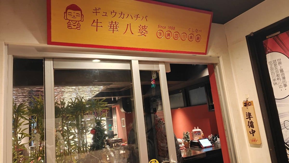 Restaurant entrance with red sign and glass doors, festive decor inside.