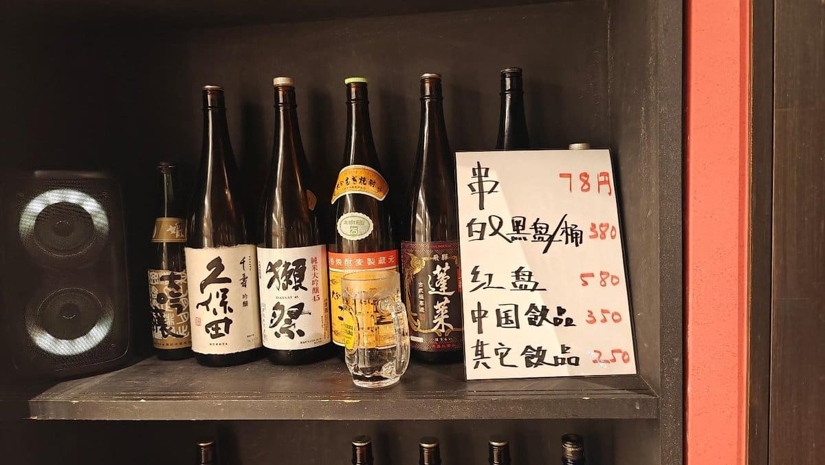 Sake bottles on shelf beside handwritten menu, warm ambient lighting.