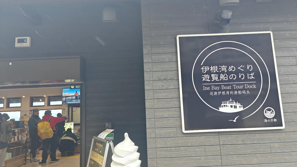 Sign for Ine Bay Boat Tour Dock with people inside ticket office.