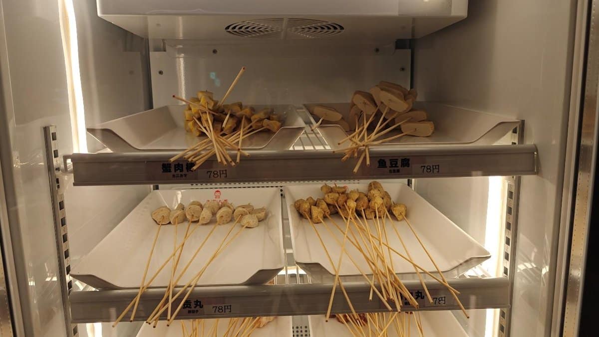 Skewers displayed in refrigerated case on white trays, labeled with prices.