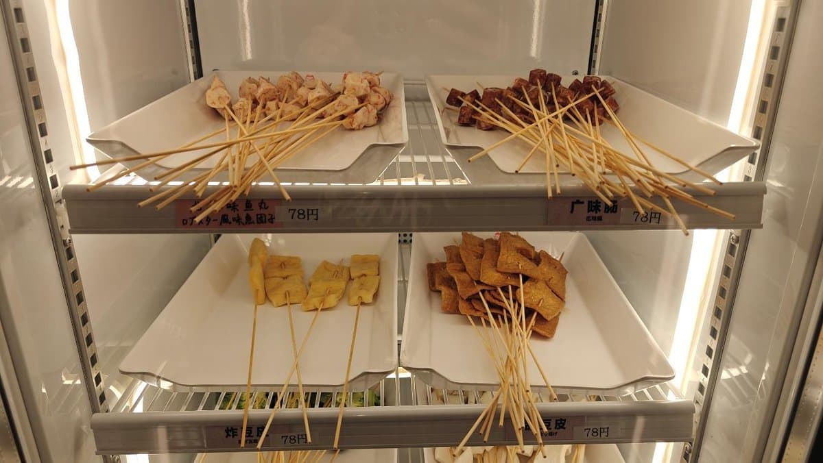 Skewers of assorted meats and tofu displayed on white trays.