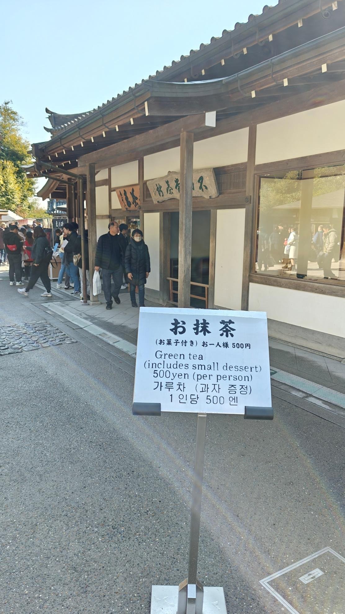 Tea house with sign offering green tea for 500 yen, people waiting.