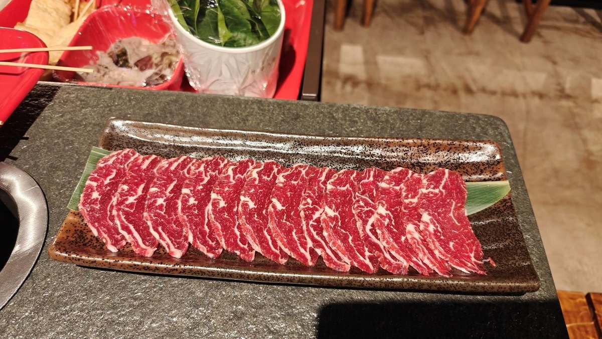 Thinly sliced raw beef on a rectangular brown plate with green leaf.