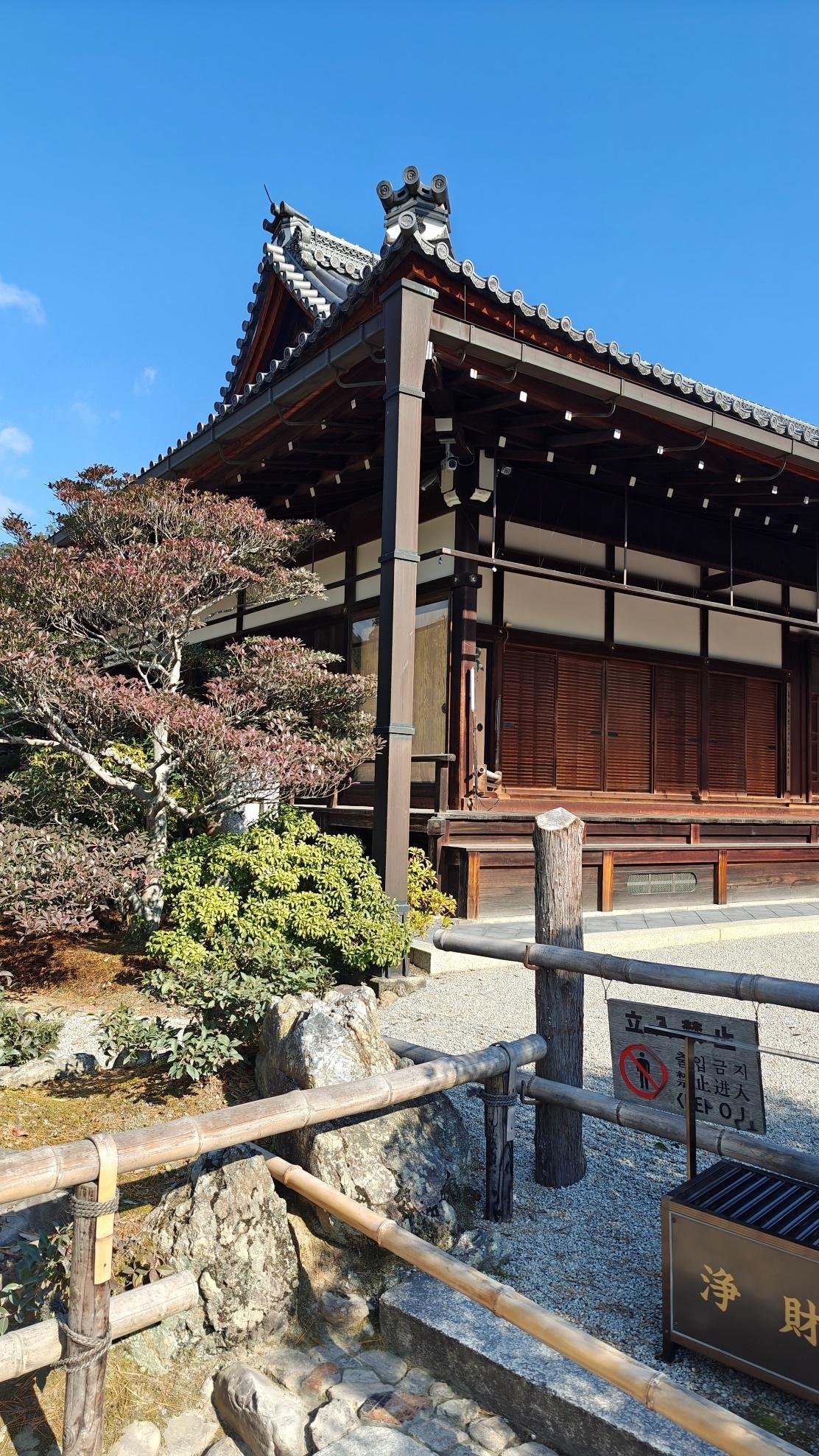 Traditional Japanese wooden building with garden under clear blue sky.