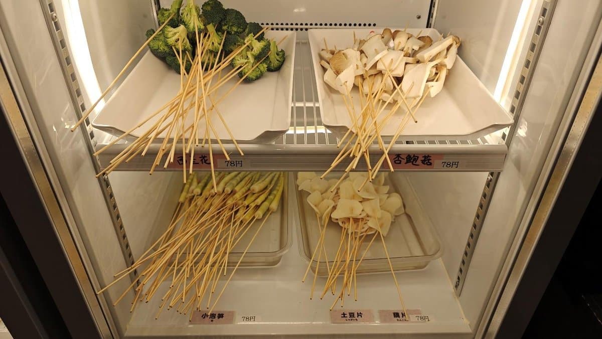 Vegetables and mushrooms on skewers in a refrigerated display.