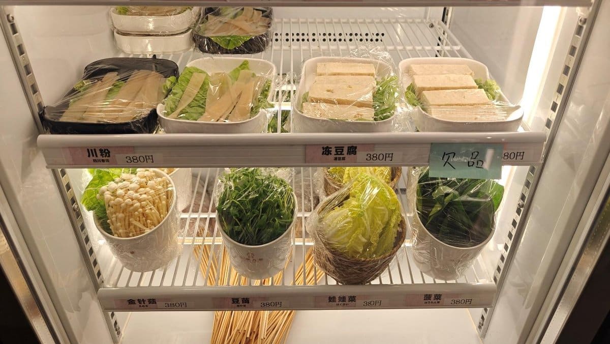 Vegetables and tofu wrapped in plastic on a refrigerator shelf.