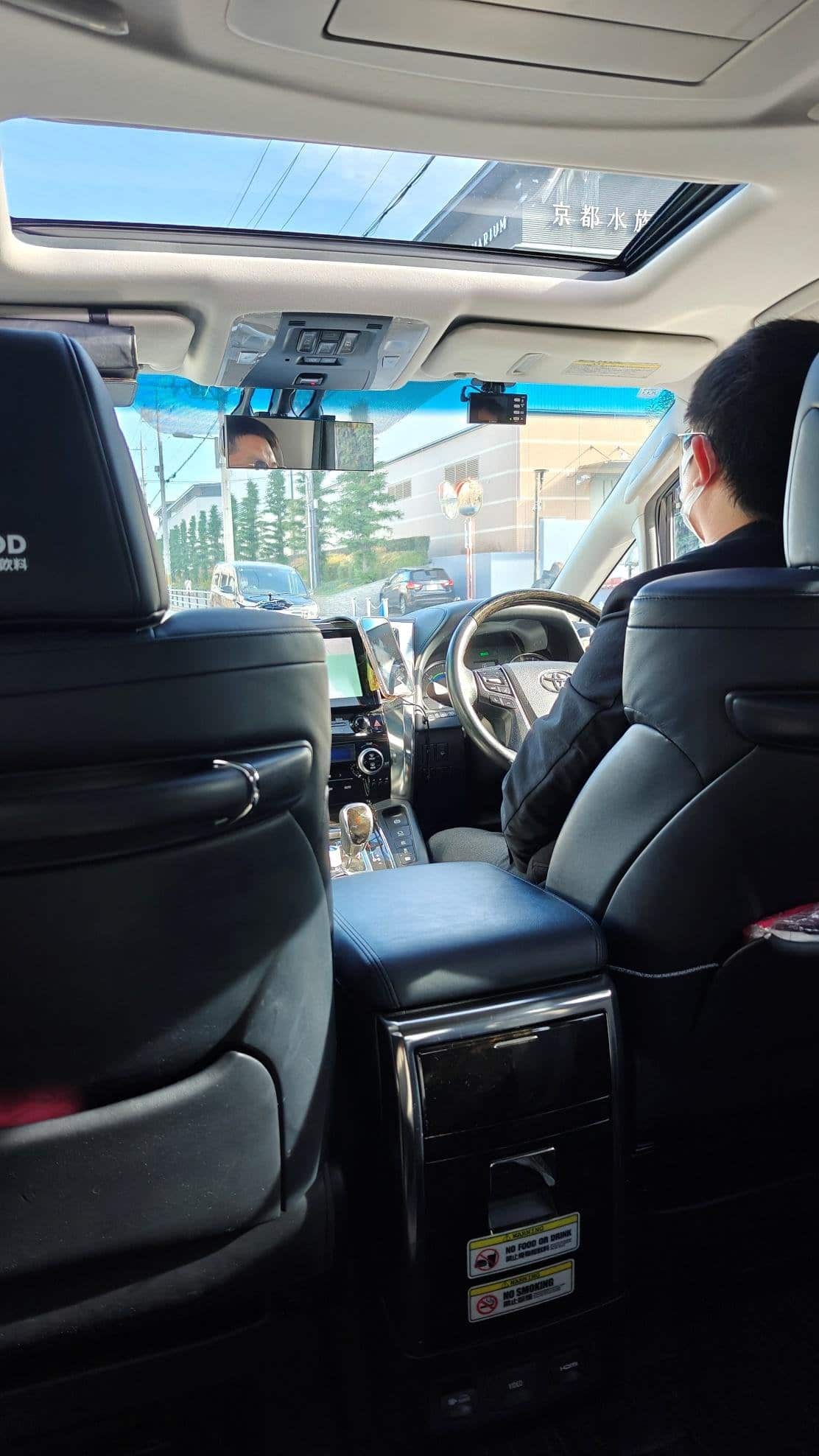 View of car interior, driver with mask, sunlight through sunroof.