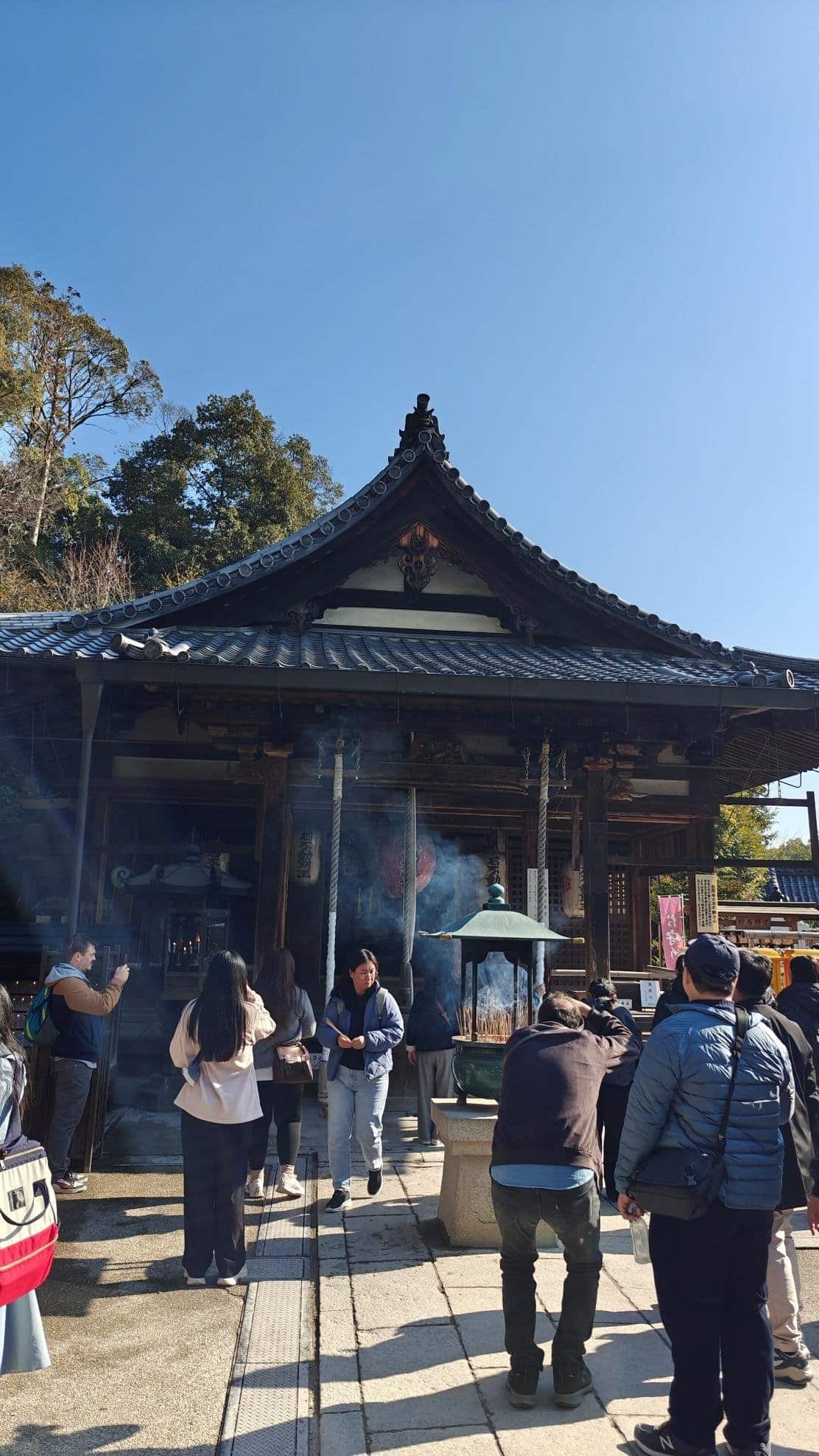 Visitors at traditional temple with incense and clear blue sky.