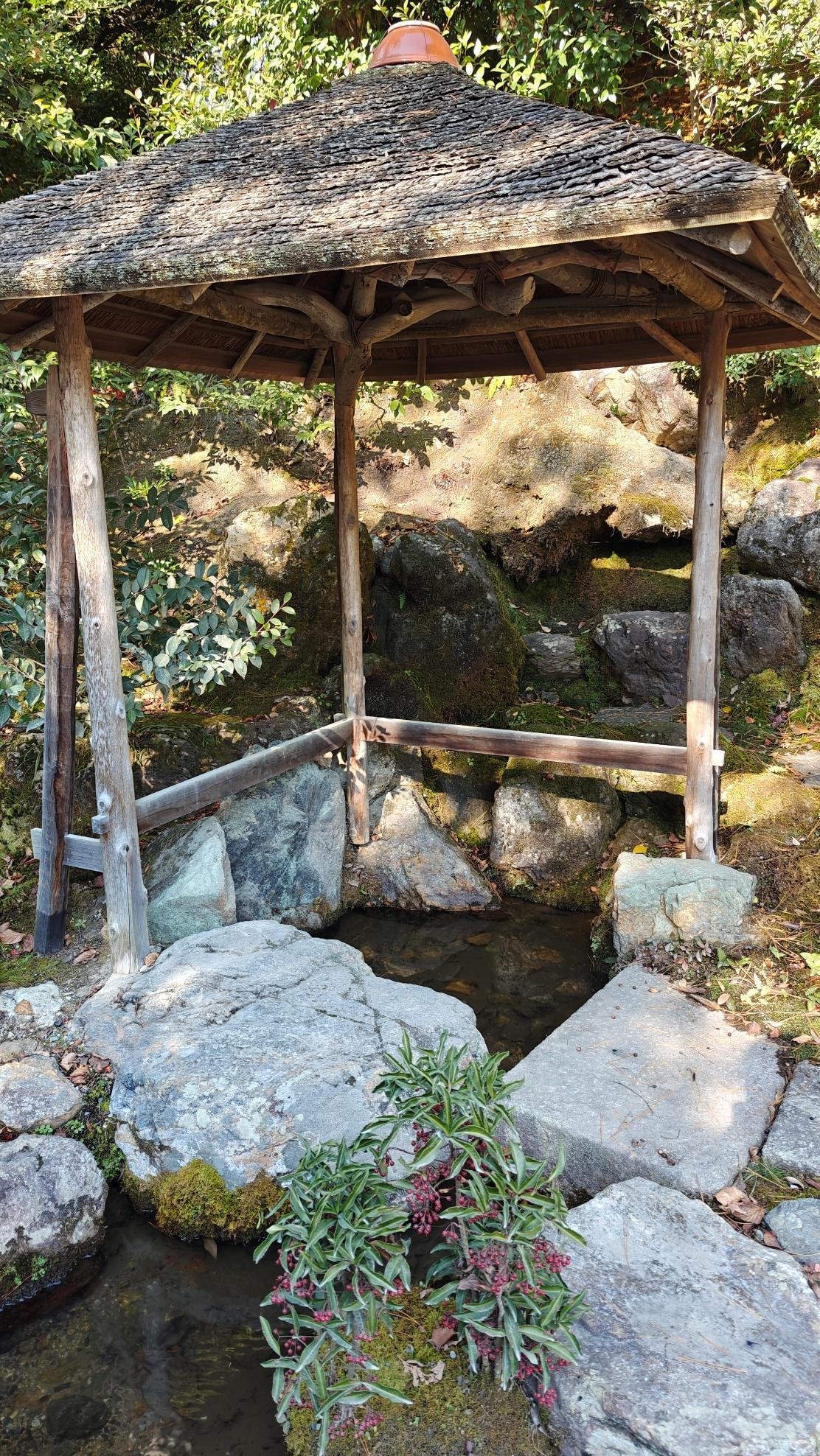 Wooden gazebo over rocks with greenery, calm and serene setting.