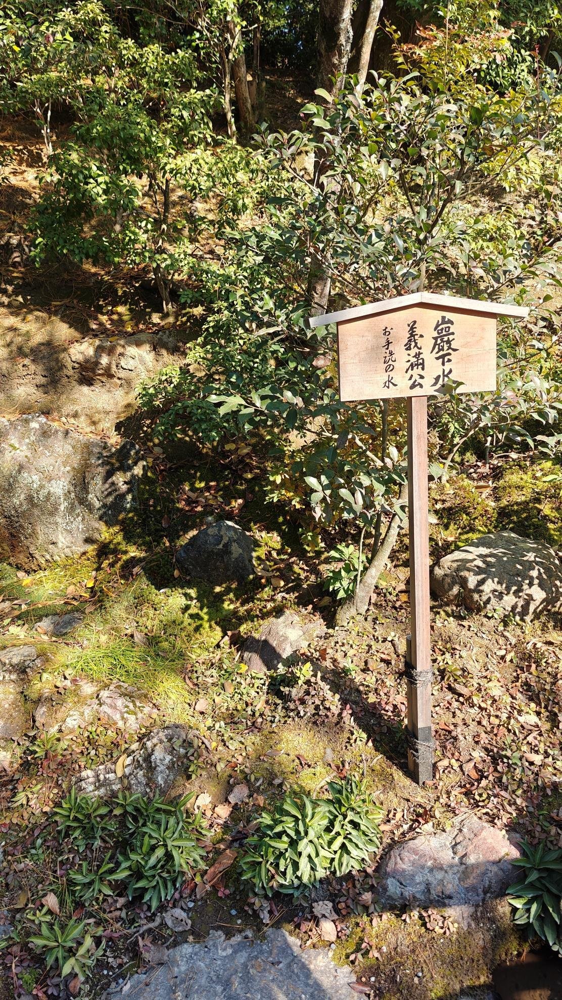 Wooden sign with Japanese text in a lush garden setting.