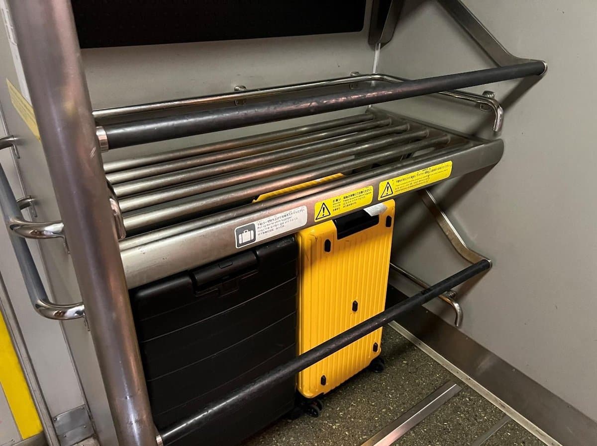 Yellow and black suitcases on train luggage rack with safety signs.